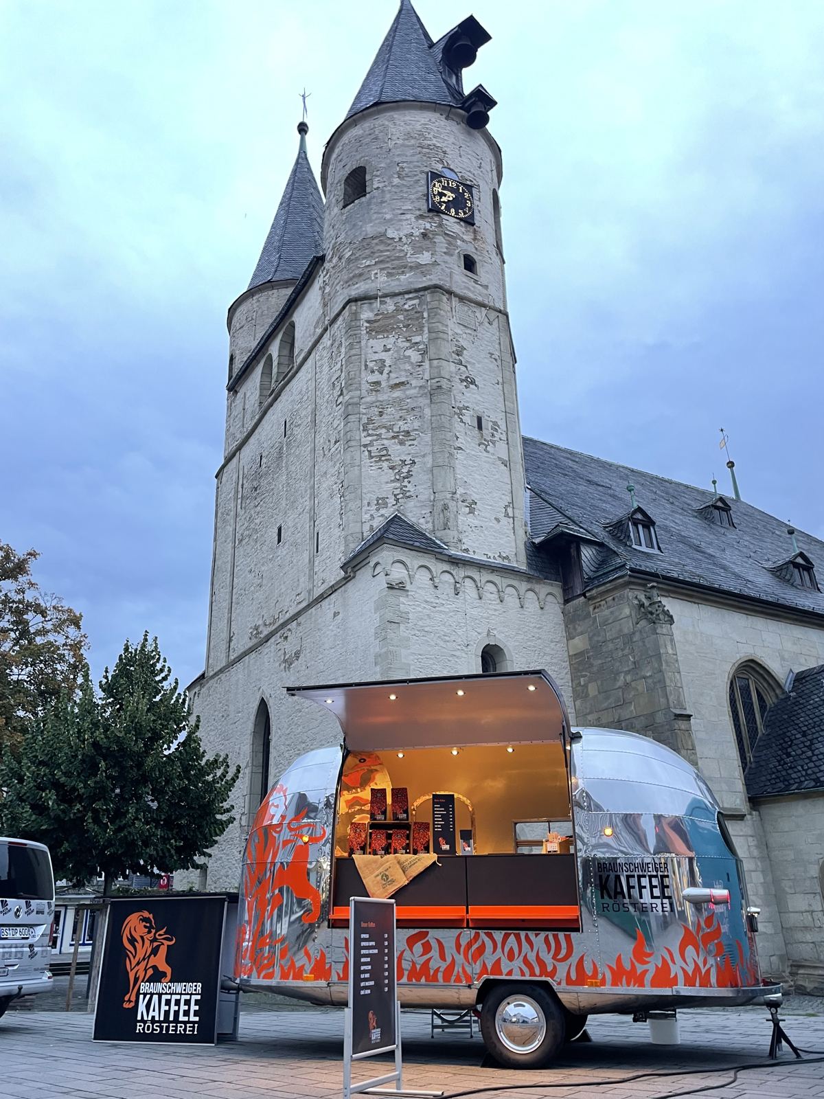 Beleuchteter Coffee Liner 48 mit Löwen-Branding in der Abenddämmerung vor einer historischen Kirche